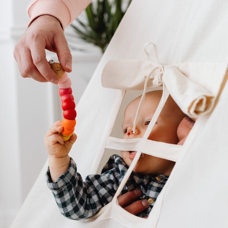 A parent shares a joyful moment with a baby, playing with a colorful toy in a cozy tent.